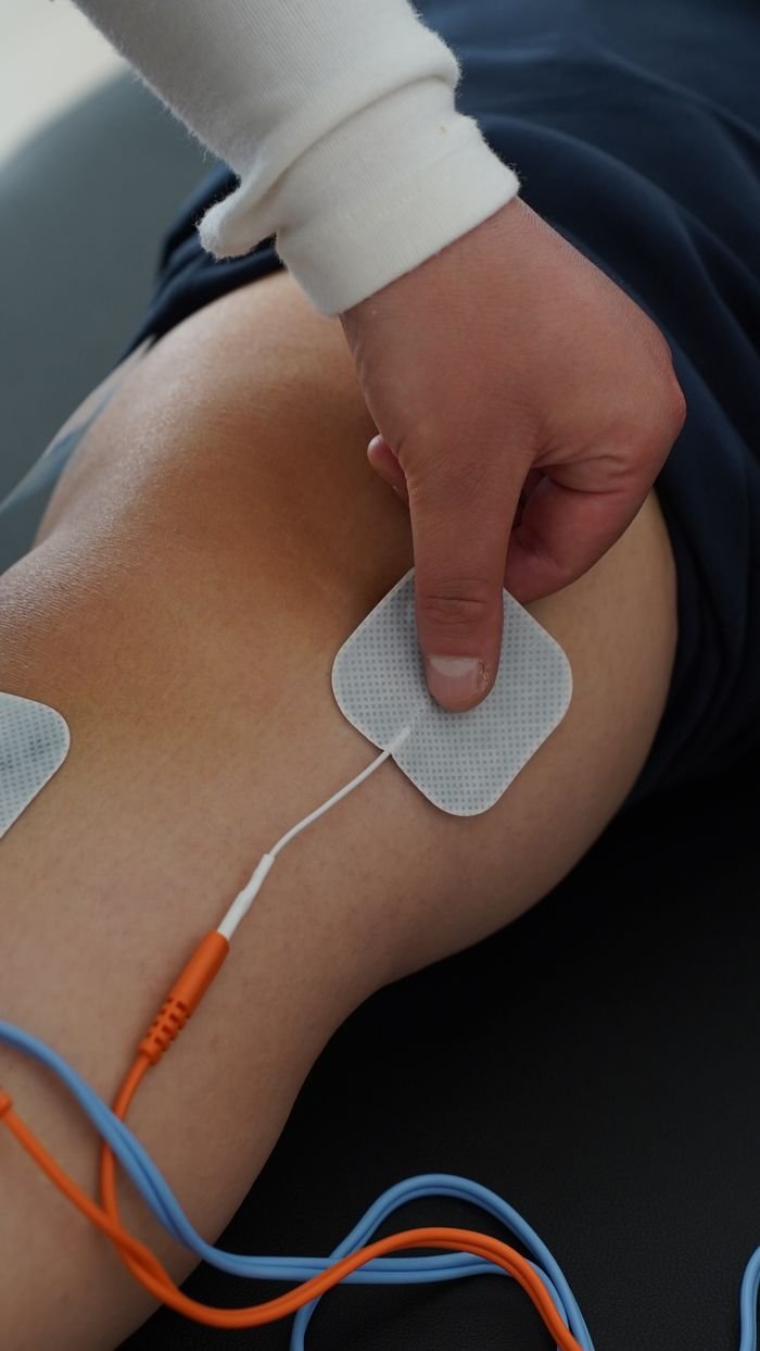 Close-up view of a person using electrical stimulation pads on the knee for therapy.